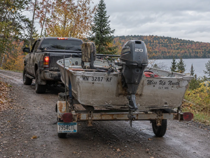 Stern of an aluminum fishing boat on a trailer beside a wooded lake