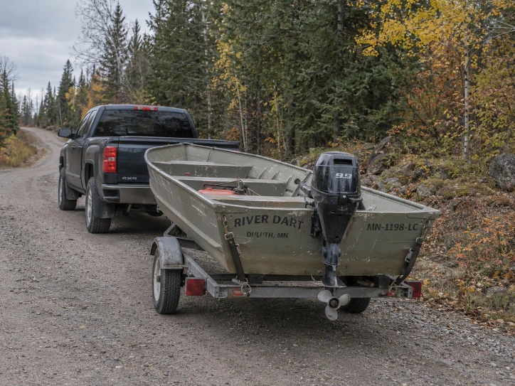 Aluminum outboard boat on a trailer along a gravel road through trees