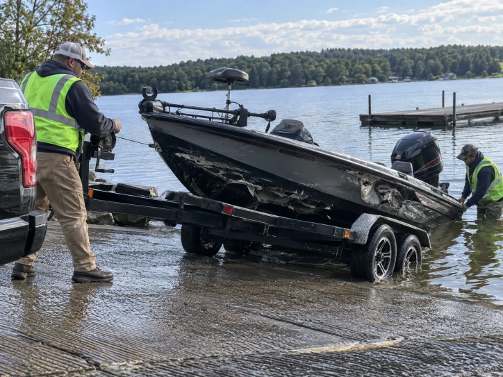 Workers beside a dark fishing boat on a trailer at a concrete launch ramp