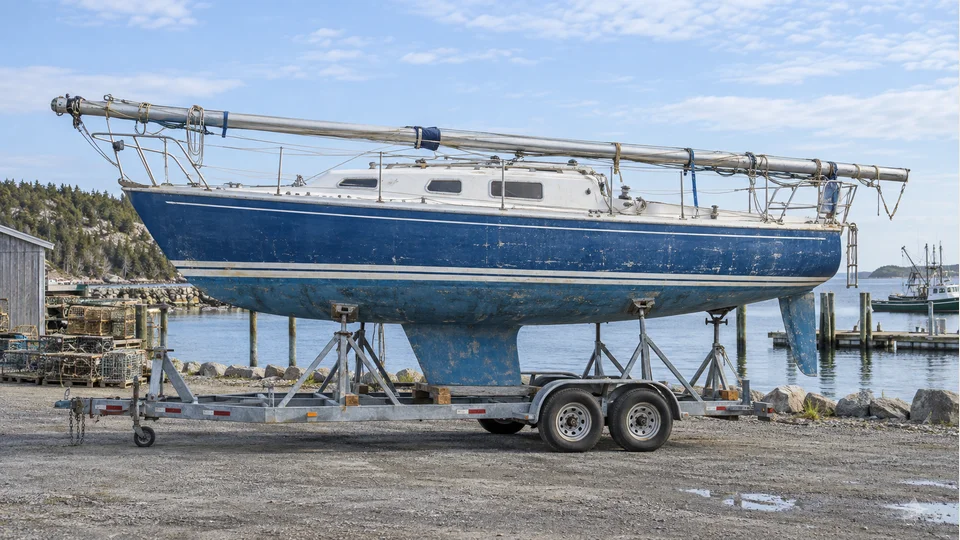Blue and white sailboat secured on a trailer with its mast lowered along the deck Illustration of blue and white sailboat secured on a trailer with its mast lowered along the deck