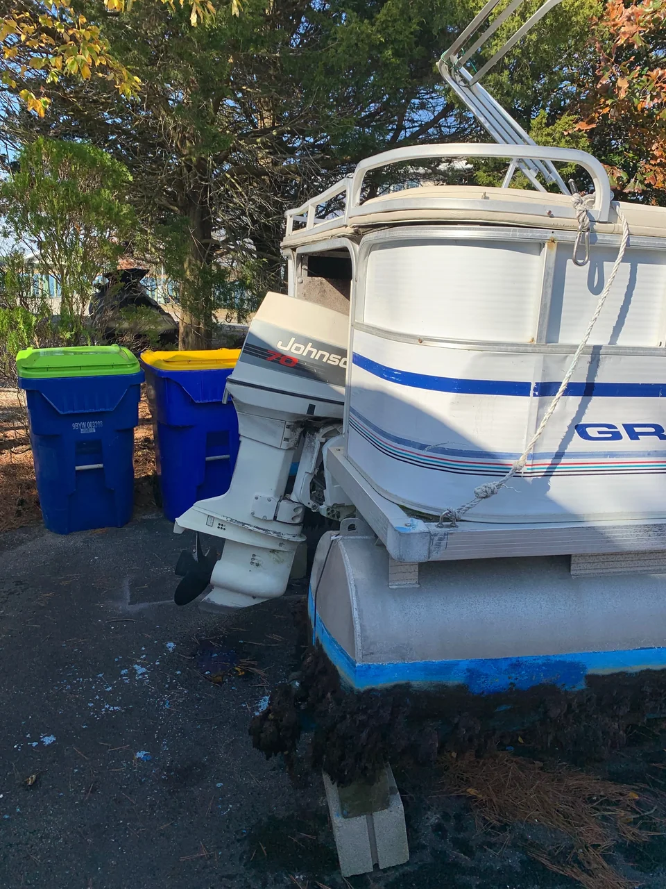 Blue-trimmed stern of a cabin boat parked beside recycling bins