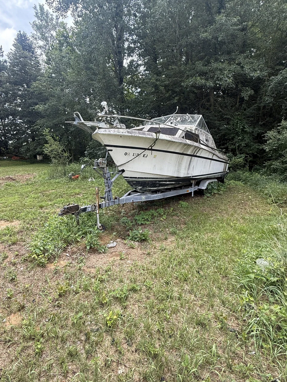Cabin boat on a trailer at the edge of an overgrown lawn