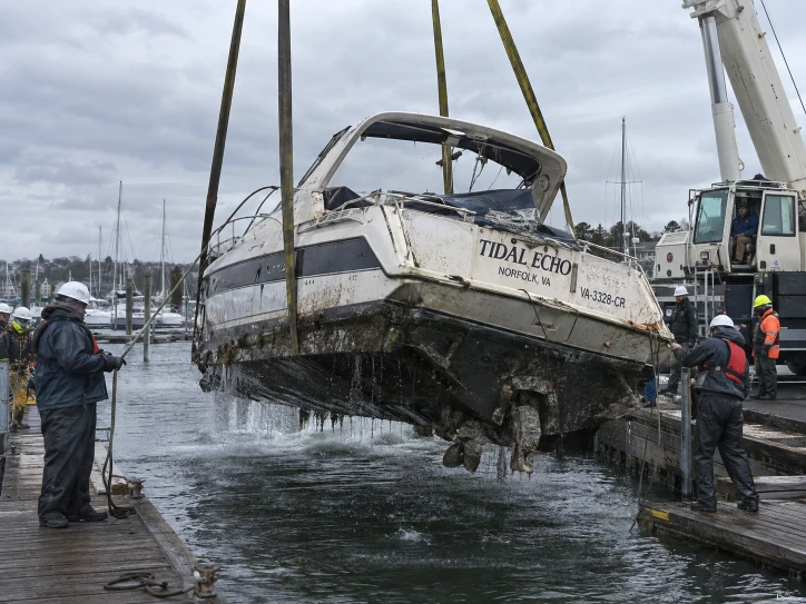 Cabin boat hanging in yellow lifting straps above the water between dock walkways