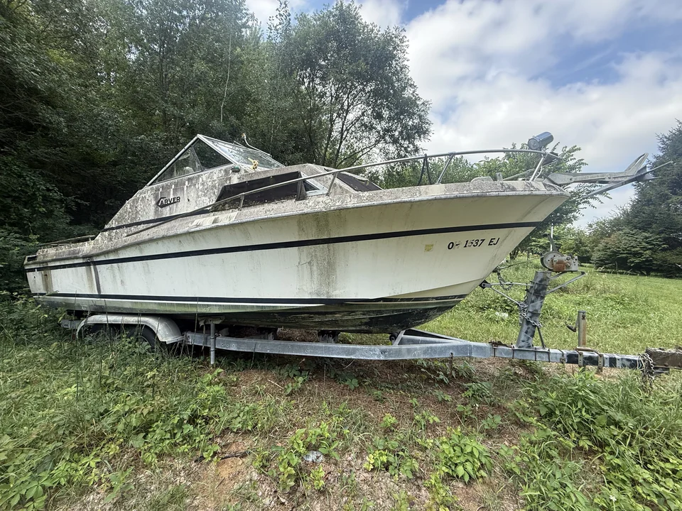 Pale green-striped cabin boat on a trailer in tall grass