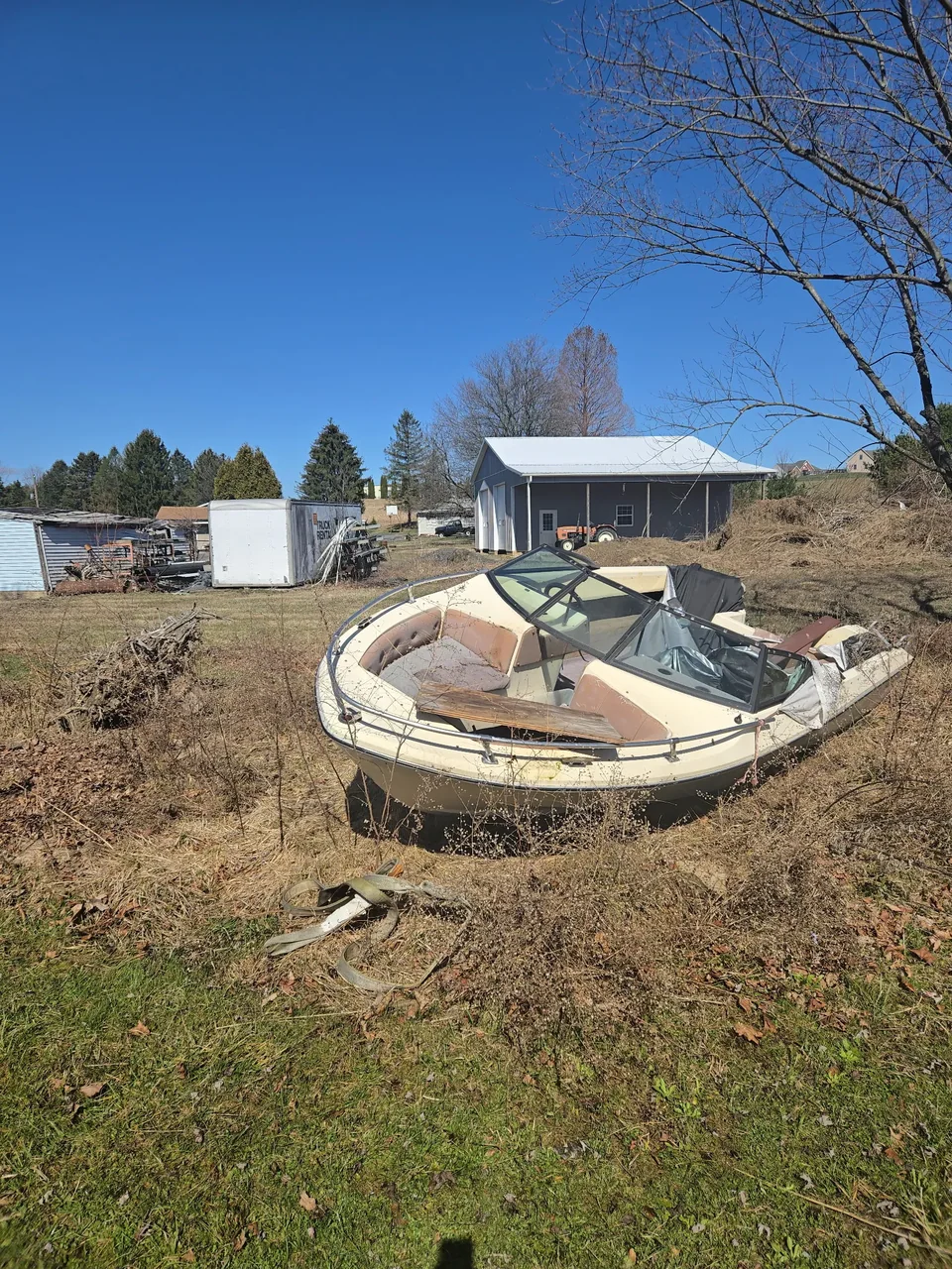 Small open hull resting in a dry field near outbuildings