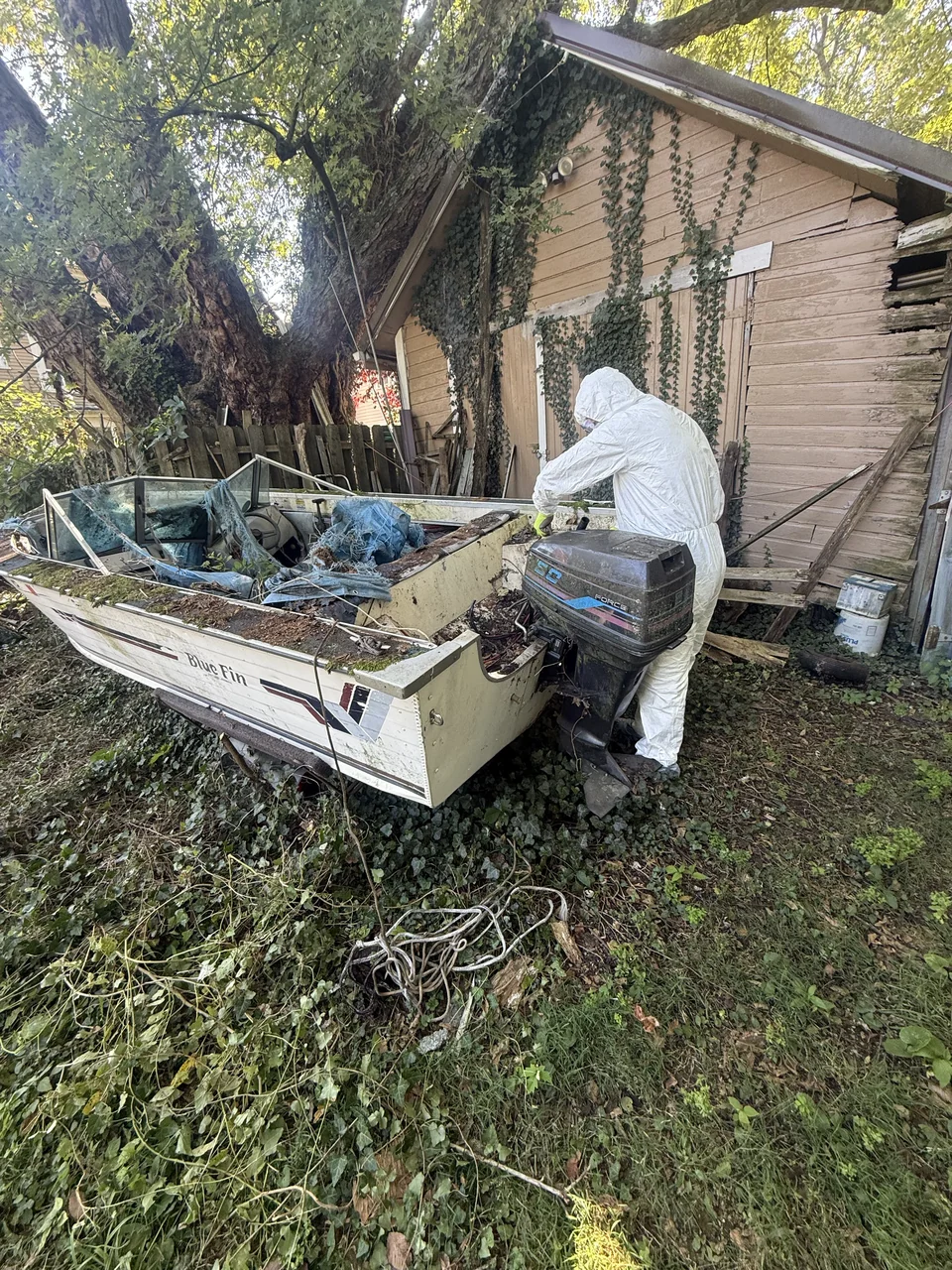 Small outboard boat stored beside a wooden shed and tree