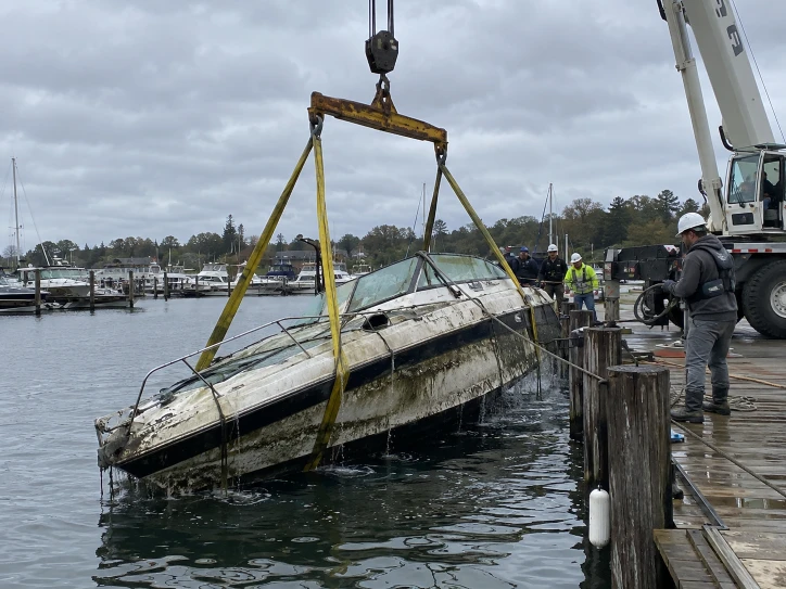 Yellow lifting straps around a low-sitting cabin boat beside a dock and crane
