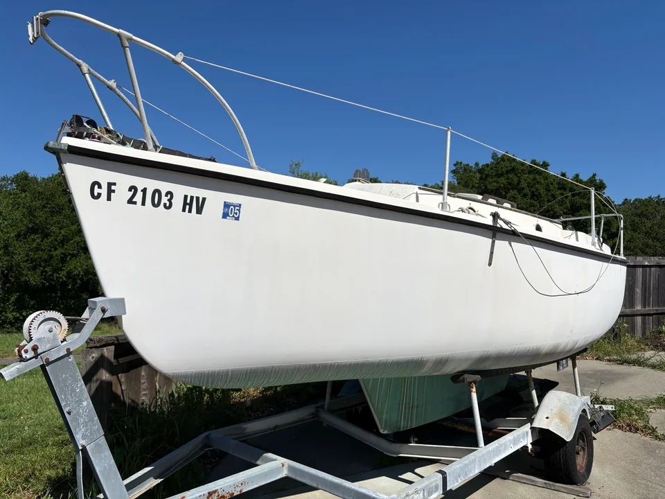 White sailing hull supported by a road trailer under a clear sky